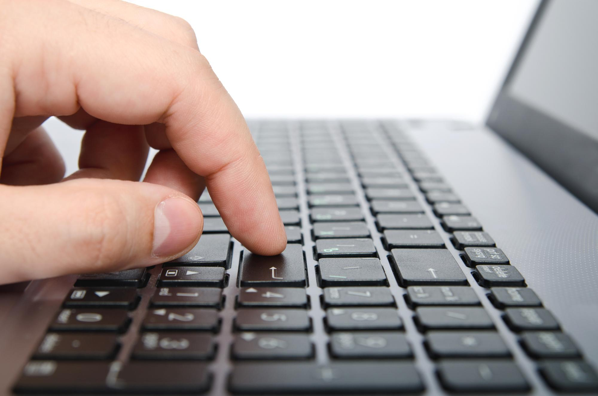 Uma mão pressionando a tecla Enter em uma teclado de laptop.